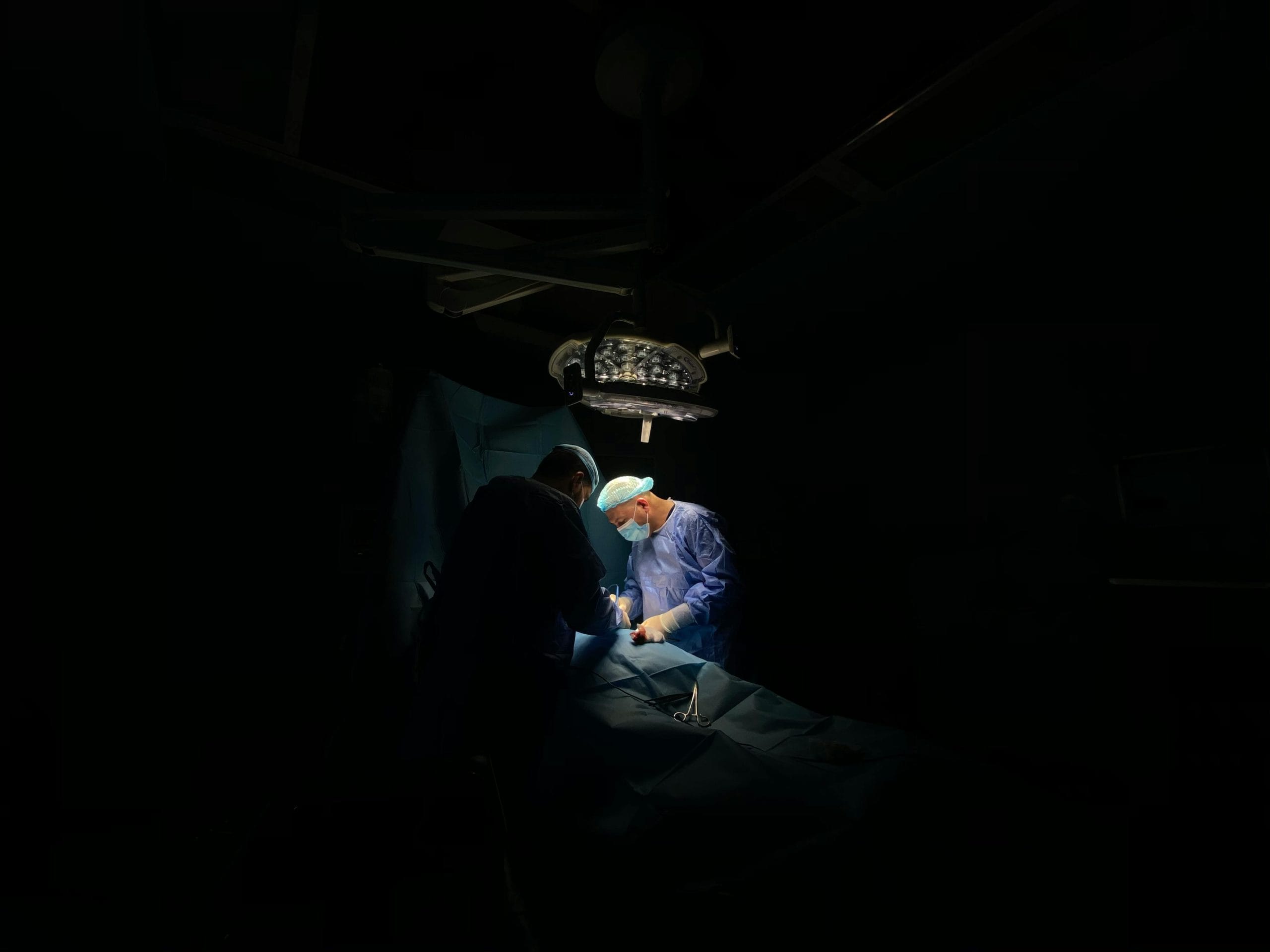 Two surgeons focus intently on a medical operation under surgical lights.