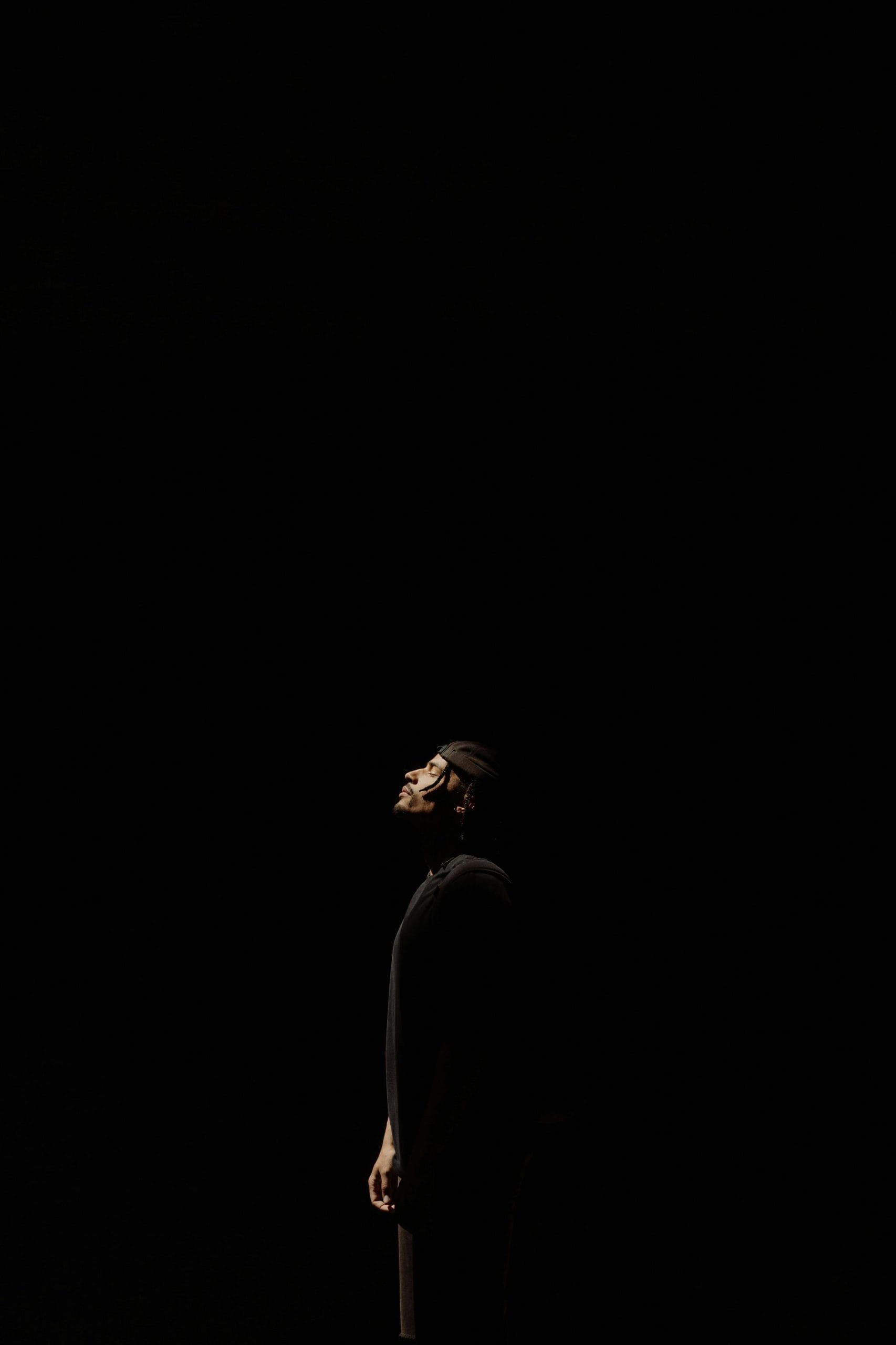 Silhouette of a man looking upwards in a dark setting with dramatic lighting.